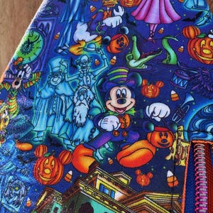 Może przedstawiać: Niebieska tkanina z nadrukiem o tematyce Halloween z Myszka Miki, Kaczorem Donaldem i innymi postaciami. Projekt zawiera dynie, duchy i nawiedzony dom. Widoczny jest czerwony zamek błyskawiczny.
