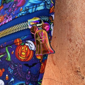 Może przedstawiać: Zbliżenie niebieskiej tkaniny z nadrukiem o tematyce Halloween, przedstawiającym dynie, duchy i inne upiorne postacie. Widoczny jest niebieski zamek błyskawiczny z metalicznym, iryzującym uchwytem zamka błyskawicznego w kształcie ducha Myszki Miki.