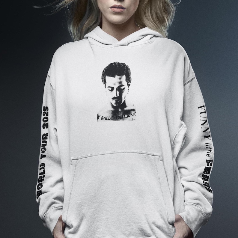 K&ouml;nnte beinhalten: Cremefarbener Kapuzenpullover mit einem Schwarz-Wei&szlig;-Portr&auml;t auf der Vorderseite. Die &Auml;rmel zeigen den Text "WORLD TOUR 2025" und "FUNNY little FEARS" in Schwarz. Der Kapuzenpullover hat eine Vordertasche und eine Kapuze mit Kordelzug.
