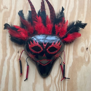 May include: A black masquerade mask with red and black feathers, red and black beads, and red rhinestones.