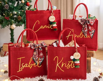 May include: Four red rectangular tote bags with two handles each, personalized with yellow cursive names Camila, Andrew, Isabel, and Kristin. Two bags feature patterned fabric bows, while two include round wooden tags with colorful tassels.