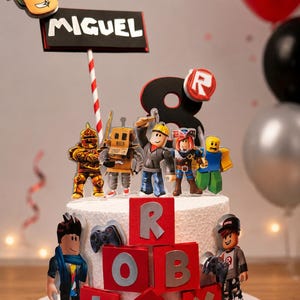 Könnte beinhalten: Eine weiß glasierte Torte, verziert mit Roblox-Figuren und roten Blöcken mit der Aufschrift "ROBLOX". Die Torte ist mit einem Schild mit der Aufschrift "MIGUEL" und der Zahl "8" versehen. Ballons in Rot, Schwarz und Silber sind im Hintergrund.
