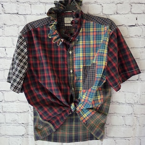 May include: A short-sleeve button-down shirt featuring a patchwork design of various plaid patterns in red, blue, yellow, green, and black. The shirt includes a ruffled collar, a front button closure, and a tie-front hem detail at the waist.