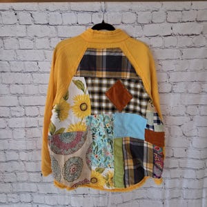 Pu&ograve; includere: Giacca patchwork con corpo in maglia waffle gialla e maniche lunghe. La schiena presenta una variet&agrave; di toppe in tessuto, tra cui girasoli, quadri e motivi floreali. Una toppa a forma di diamante marrone &egrave; centrata sul retro.