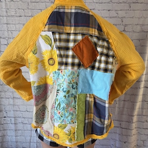 Pu&ograve; includere: Una giacca patchwork con maniche gialle e varie toppe di tessuto. Le toppe includono motivi floreali, a quadri e colori uniti come blu, verde e marrone. La giacca ha un orlo sfilacciato e un collo alto.
