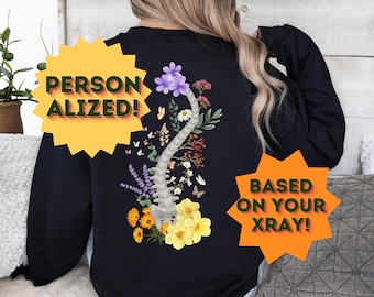 Pode incluir: Camisola preta com um design floral que apresenta uma coluna vertebral e o texto "Personalizado! Com base no seu raio-x!"
