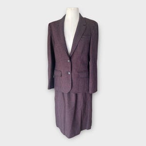 May include: A two-piece suit set featuring a blazer and a matching skirt in a dark purple and black micro-check pattern. The blazer has a notched lapel, long sleeves, two front buttons, and two flap pockets. The skirt is a straight, knee-length cut.