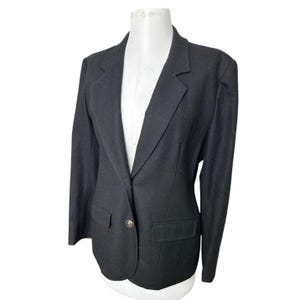 Op de afbeelding: Een zwarte blazer met een enkele knoopsluiting en twee voorzakken. De blazer wordt getoond op een witte mannequin. Het ontwerp omvat een revers met inkeping en lange mouwen. De stof lijkt een effen, donkere kleur te hebben.