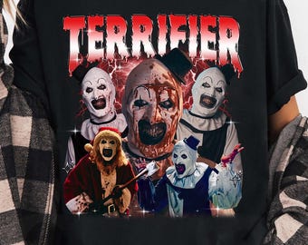 May include: Black t-shirt featuring the word "TERRIFIER" in red, above a graphic of several scary clowns. The clowns have white faces, black and white outfits, and menacing expressions. The shirt is a casual style.