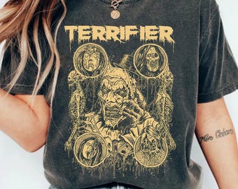 May include: Dark gray t-shirt featuring the word "TERRIFIER" in yellow block letters above a graphic of a scary clown and other horror characters. The shirt has a vintage, worn look.