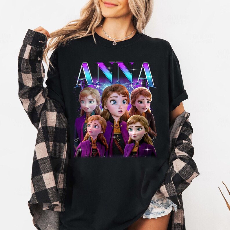 Puede incluir: Camiseta negra con el nombre "ANNA" en una fuente vibrante y degradada. La camiseta muestra un gr&aacute;fico del personaje Anna de la pel&iacute;cula animada, con m&uacute;ltiples im&aacute;genes de ella en varias poses. El dise&ntilde;o tiene un esquema de color p&uacute;rpura y azul.