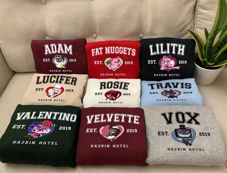 May include: Nine different colored sweatshirts with cartoon character graphics and the text "Hazbin Hotel" on each. The characters include Adam, Fat Nuggets, Lilith, Lucifer, Rosie, Travis, Valentino, Velvette, and Vox.