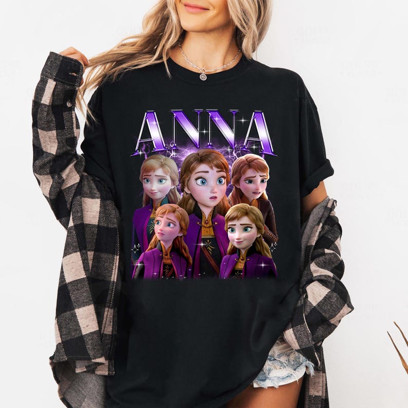 Puede incluir: Camiseta negra con la palabra "ANNA" en fuente morada estilizada. Debajo, un gr&aacute;fico de cinco personajes animados con atuendos morados y marrones.