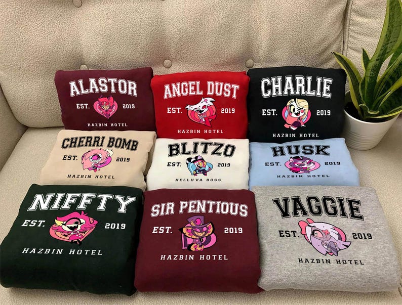 May include: Nine different colored sweatshirts with cartoon characters and text. The text on the sweatshirts reads "ALASTOR EST. 2019 HAZBIN HOTEL", "ANGEL DUST EST. 2019 HAZBIN HOTEL", "CHARLIE EST. 2019 HAZBIN HOTEL", "CHERRI BOMB EST. 2019 HAZBIN HOTEL", "BLITZO EST. 2019 NELLUVA BOSS", "HUSK EST. 2019 HAZBIN HOTEL", "NIFFTY EST. 2019 HAZBIN HOTEL", "SIR PENTIOUS EST. 2019 HAZBIN HOTEL", and "VAGGIE EST. 2019 HAZBIN HOTEL".