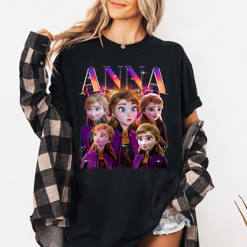 Puede incluir: Camiseta negra con la palabra "ANNA" en una fuente colorida y estilizada. La camiseta muestra un gr&aacute;fico de cinco personajes animados con piel clara, vestidos con trajes morados y dorados. Los personajes tienen diferentes expresiones y peinados.