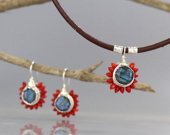 May include: A silver necklace and earrings set with a blue gemstone surrounded by red coral beads. The necklace is on a brown leather cord.