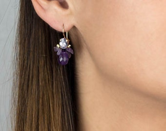 May include: Amethyst and clear crystal dangle earrings with a gold tone finish.