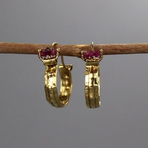 May include: Gold hoop earrings with a hammered texture and small red gemstones at the top.