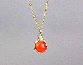 May include: A gold chain necklace with a red gemstone pendant. The pendant is wrapped in gold wire and has a faceted design.