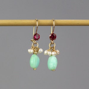 Peut inclure: Une paire de boucles d'oreilles en or avec une pierre ovale vert clair, un groupe de perles blanches et une petite pierre rouge au sommet.