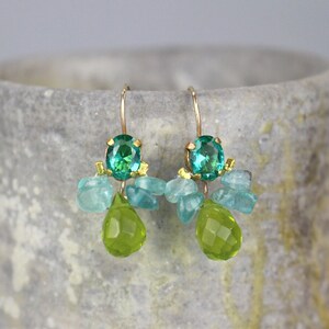 May include: A pair of gold earrings with green and blue gemstones. The earrings feature a large green gemstone surrounded by smaller blue gemstones.