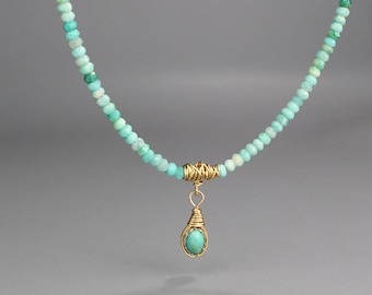 May include: A turquoise gemstone necklace with a gold wire wrapped pendant. The necklace is made of small, round turquoise beads and has a simple, elegant design.