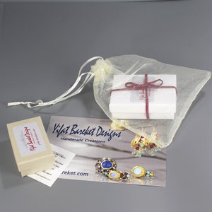 Peut inclure: Une petite bo&icirc;te blanche avec un ruban rouge autour. La bo&icirc;te est plac&eacute;e dans un sac en maille blanche. Il y a une carte de visite avec le texte "Yifat Bareket Designs Handmade Creations" et une adresse de site Web.