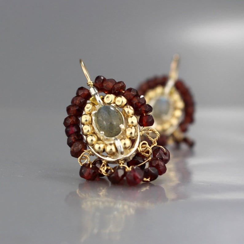 Peut inclure: Boucles d'oreilles en argent et en or avec une pierre pr&eacute;cieuse grise entour&eacute;e de petites perles dor&eacute;es et de perles de grenat rouge.