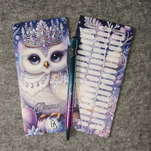 May include: A set of Diamora stickers with an owl design, a pen, and a notepad. The owl is white with blue eyes and a jeweled crown. The pen has a metallic finish with blue, purple, and green hues. The notepad has a purple and blue floral design.