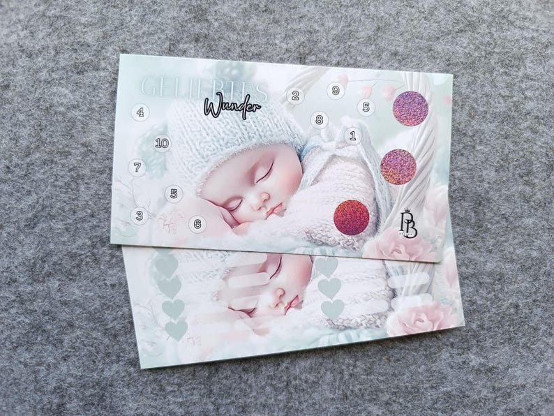 May include: A rectangular card featuring a sleeping baby in a knit hat and sweater. The card displays the text "Wunder" and "GELIEBTES", numbered circles from 1 to 10, and three circular glittery patches in pink and red tones.