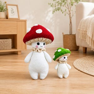 May include: Two crochet mushroom dolls. One has a red cap with white spots, the other has a green cap with white spots. Both have white bodies, smiling faces, and beige ruffs. They are standing on a wooden floor.