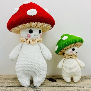 Puede incluir: Dos peluches de hongo tejidos a crochet. El más grande tiene un gorro rojo y blanco y el más pequeño tiene un gorro verde. Ambos tienen cuerpos blancos y caras sonrientes.