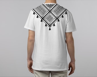 May include: White t-shirt with a black and white geometric pattern on the back, featuring a square design with tassels. The shirt is short-sleeved and has a crew neck.