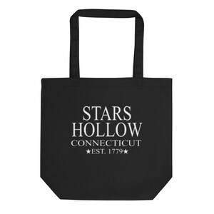 May include: Black tote bag with white text that reads "STARS HOLLOW CONNECTICUT EST. 1779". The bag has two handles and is made of a sturdy material. The design is centered on the front of the bag.