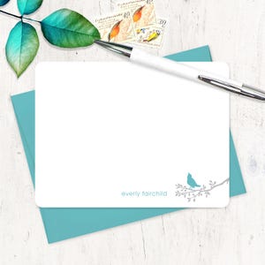 May include: A white card with a blue bird on a branch in the bottom right corner. The card has the text "everly fairchild" printed in gray at the bottom. The card is sitting on a blue envelope.