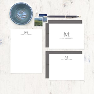 May include: Two sets of personalized stationery with a gray envelope. The stationery is white with a gray letter "M" and the name "John Matthews" printed at the top.