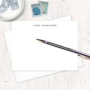 May include: A white card with the name "LUKE HAMILTON" printed in black at the top. A black pen with a gold tip is lying on the card.