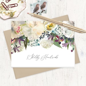 May include: A white card with a watercolor floral design in shades of pink, purple, and green. The text "Shelby Hendricks" is written in black cursive at the bottom of the card.