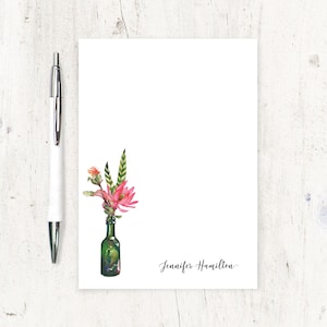 May include: A white stationery card with a green glass bottle filled with pink flowers and green leaves. The name "Jennifer Hamilton" is written in cursive at the bottom of the card.