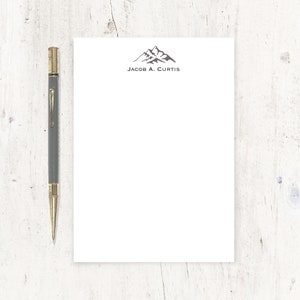 May include: A white notepad with a mountain range logo and the text "Jacob A. Curtis" printed in black at the top.