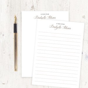 May include: Two white notepads with lined paper. The top notepad has the text "a note from Bridgette Adams" printed in brown cursive. The bottom notepad has the same text printed in brown cursive.