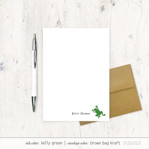 May include: A white stationery set featuring a green frog illustration and the name "Brice Thomas." Includes a matching kraft paper envelope and a silver and white pen. The ink color is Kelly green.
