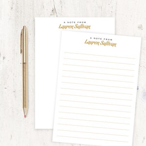 May include: Two white lined notepads with gold text that reads "A note from Lauren Sullivan".