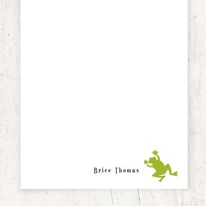 May include: White stationery with the name "Brice Thomas" printed in black. A green frog silhouette is in the lower right corner. The stationery is on a white wooden surface.