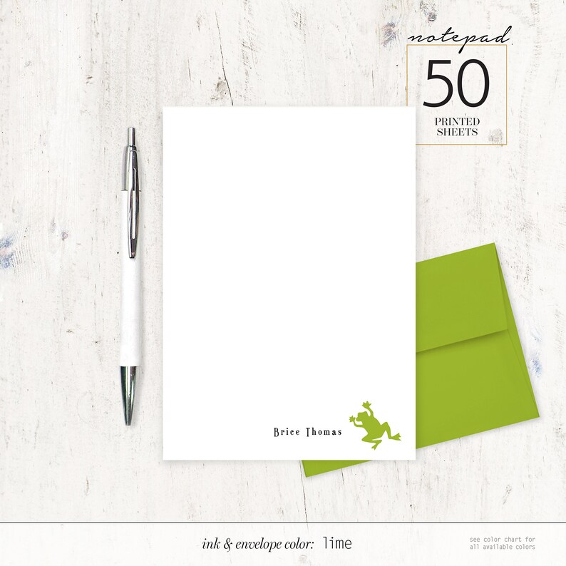 May include: White notepad with the text "Brice Thomas" and a lime green frog illustration. A lime green envelope is next to the notepad. A silver and white pen is on the left. The notepad reads "notepad 50 printed sheets".