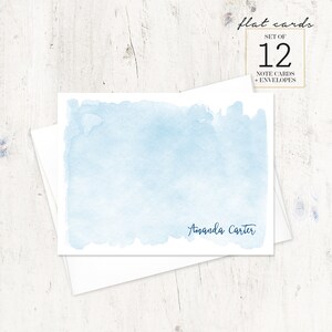 Puede incluir: Un juego de 12 tarjetas de notas de acuarela azul con sobres. Las tarjetas presentan un fondo de acuarela azul claro con el nombre "Amanda Carter" impreso en tinta azul oscuro en la parte inferior.