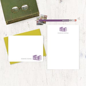 May include: A set of two blank stationery note cards with a purple illustration of stacked books. The cards have the name "elizabeth sullivan" printed on them.
