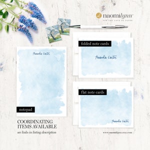 May include: A set of personalised stationery featuring a light blue watercolour background with the name "Amanda Carter" printed in black. The set includes folded note cards, flat note cards, and a notepad.
