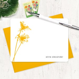 May include: A white card with a yellow floral design and the text "anne alexander" printed at the bottom.