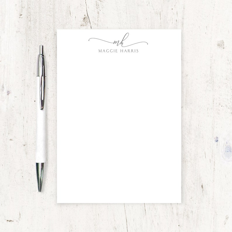 May include: White notepad with a black pen. The notepad has a black script monogram "mh" and the text "Maggie Harris" printed at the top.
